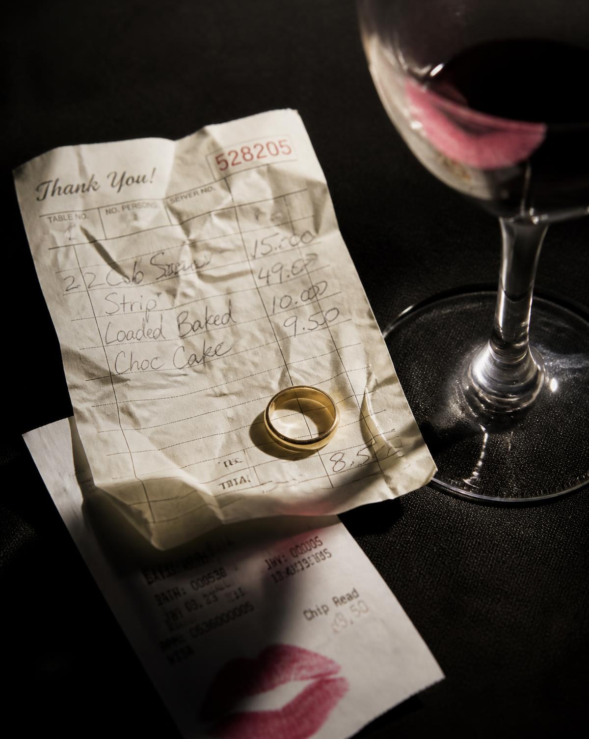 A restaurant check and a wedding band beside a wine glass