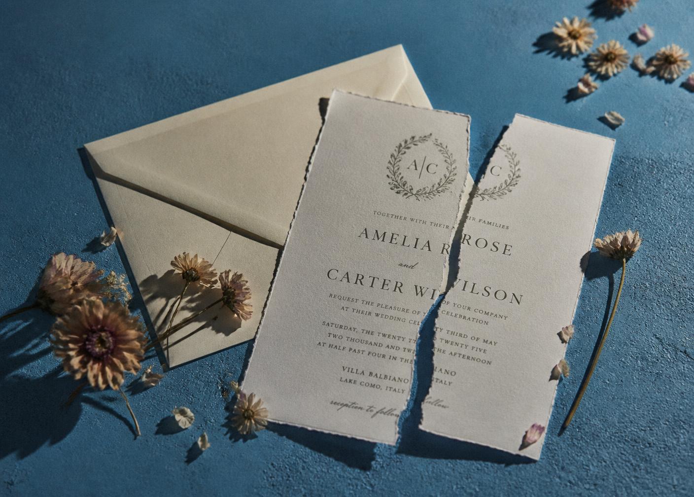 A wedding invitation torn in two beside dried flowers on a pool blue surface