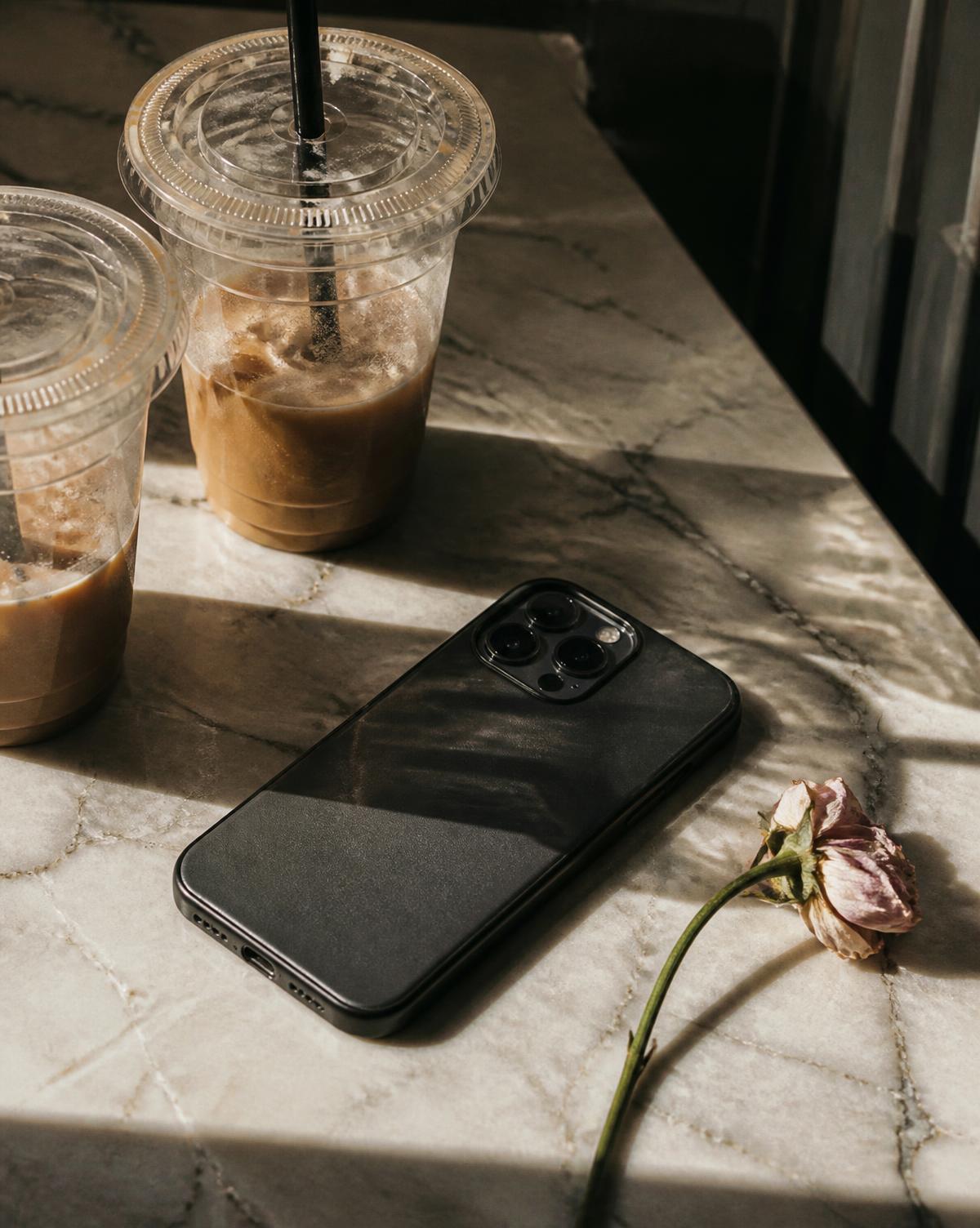 A phone face-down on a marble counter beside two cold coffees and a wilted rose